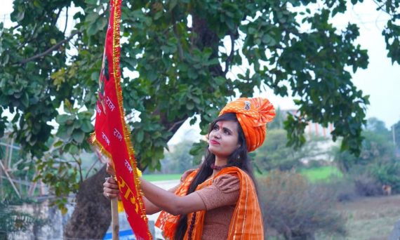 A woman in traditional Indian attire holding a decorative flag outdoors.